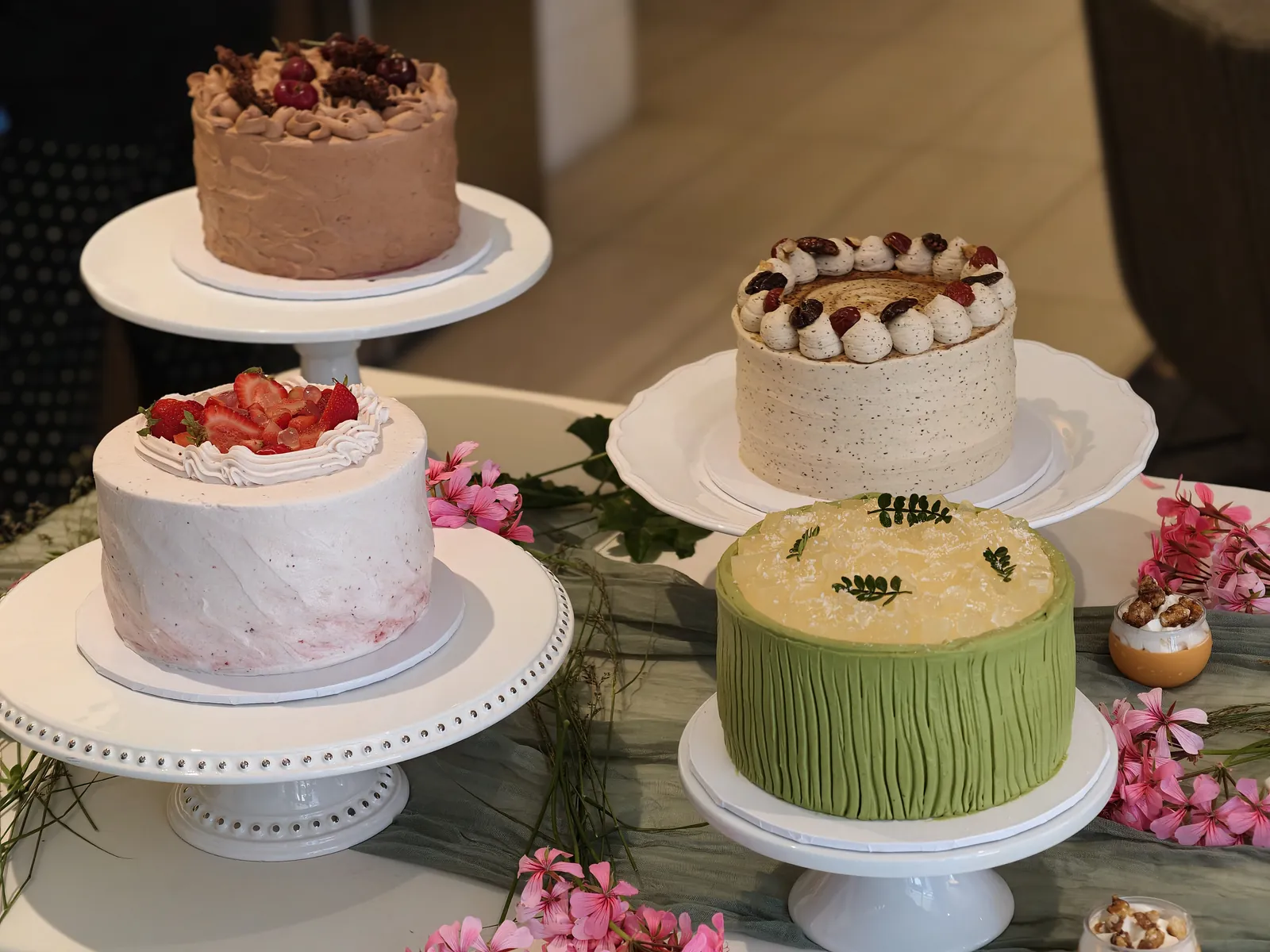 Four Yohaku Sweets cakes on white stands, including a strawberry cream cake and a green-frosted cake